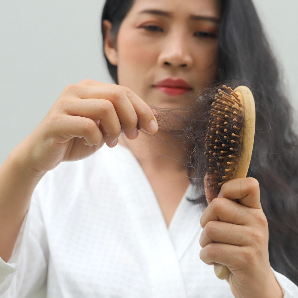 Woman experiencing hair shedding while brushing hair due to stress and daily scalp issues