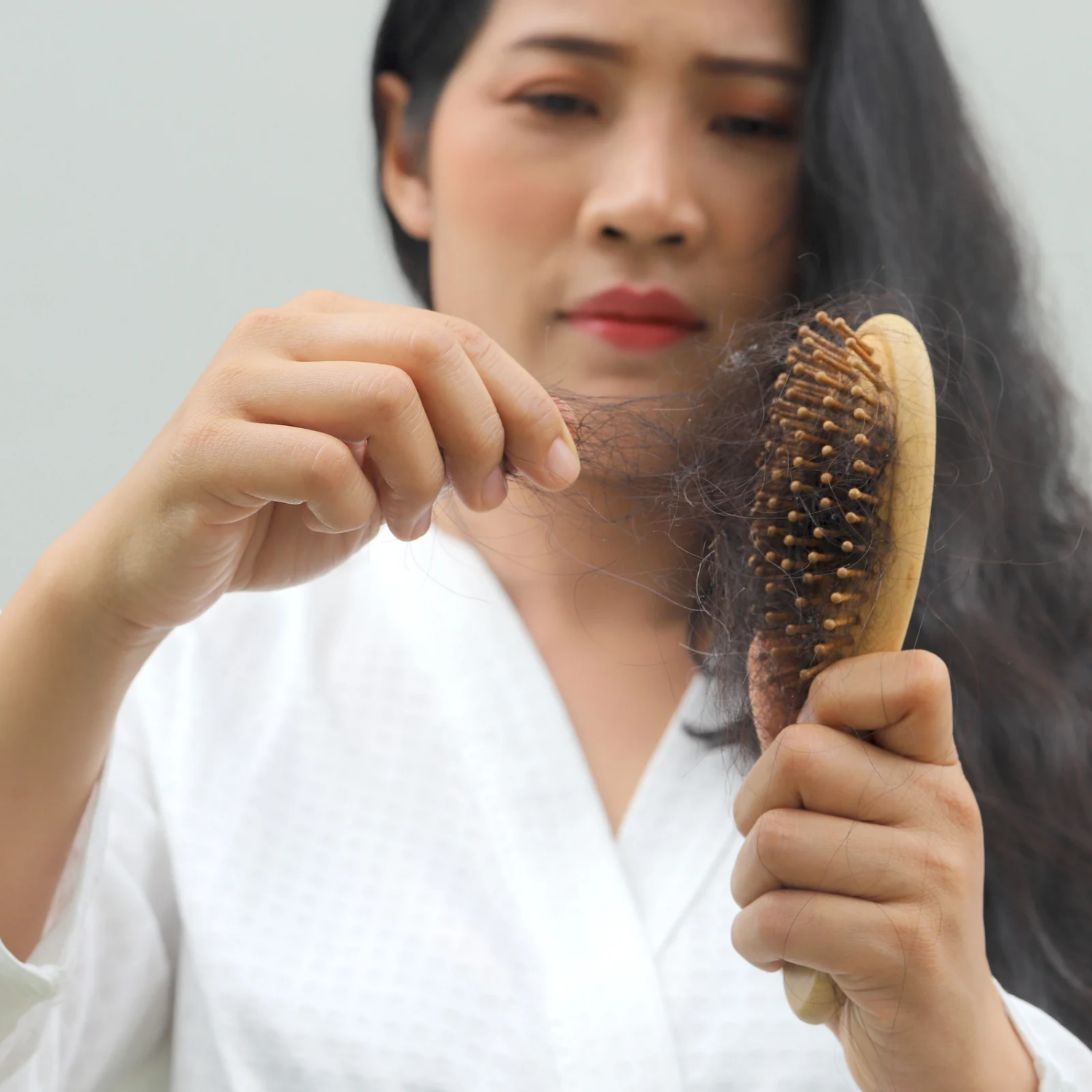 Woman experiencing hair shedding while brushing hair due to stress and daily scalp issues